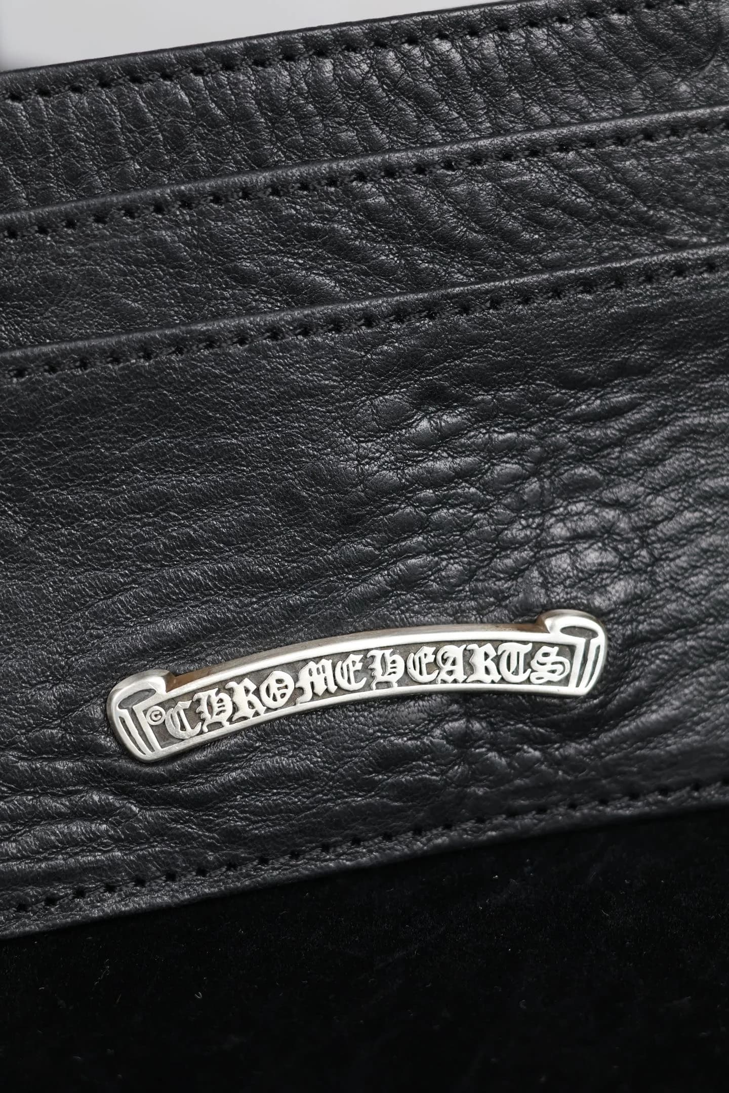Крупный план серебряного скролла Chrome Hearts на кожаном картхолдере
