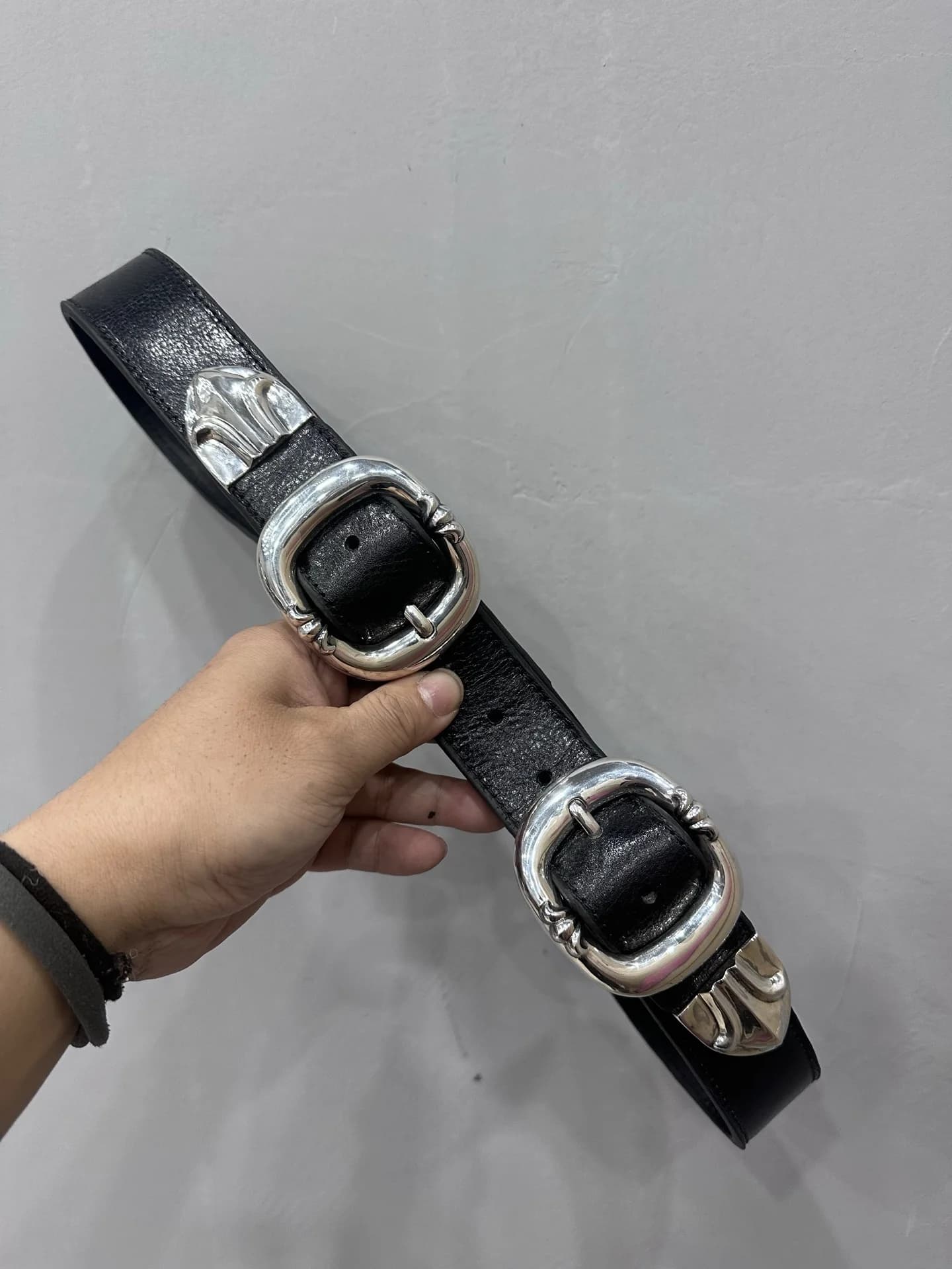 Черный кожаный ремень Chrome Hearts с двумя серебряными пряжками в руке