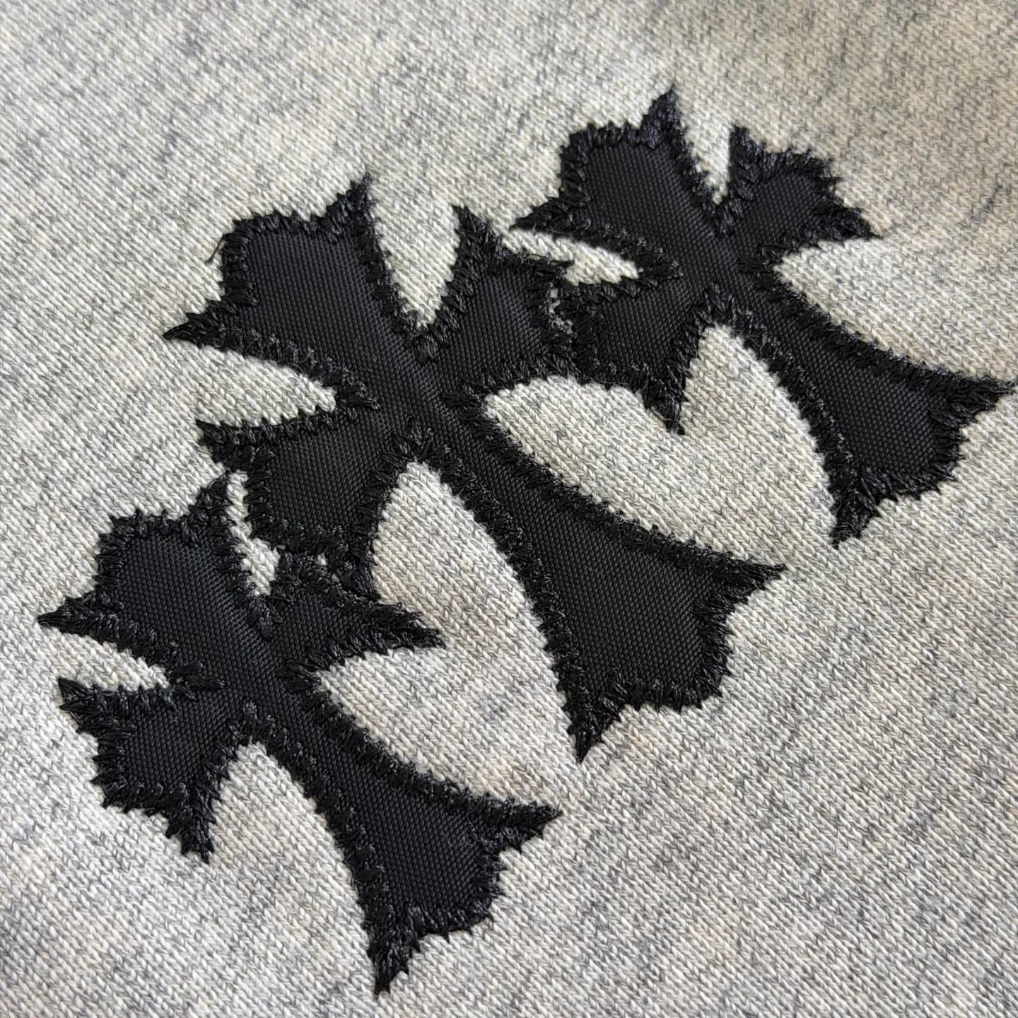 Деталь аппликации в виде трех черных крестов на груди худи Chrome Hearts