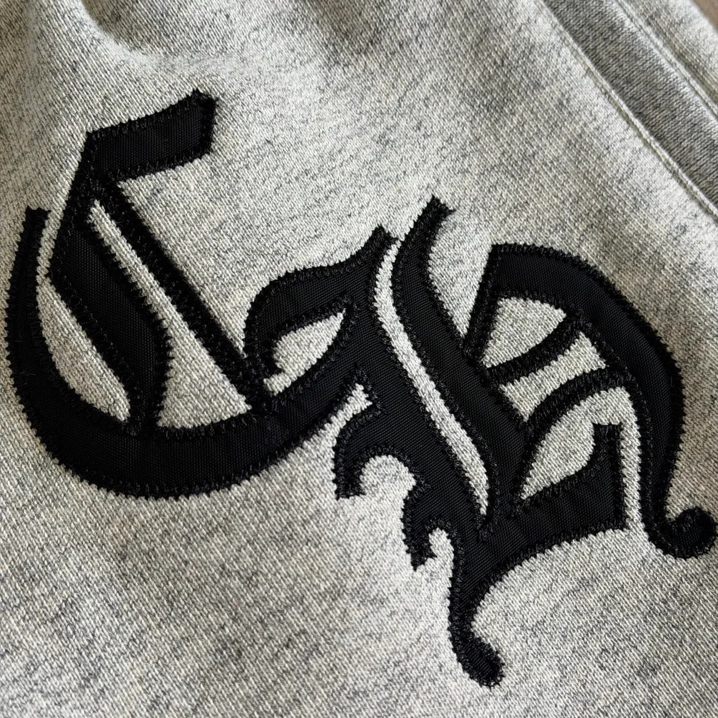 Крупный план вышивки монограммы CH на серых спортивных штанах Chrome Hearts