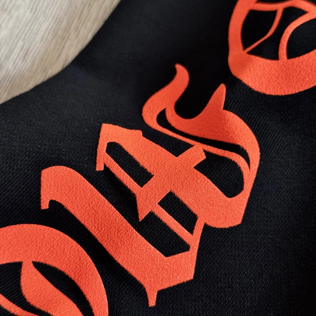 Деталь оранжевого принта с готическим шрифтом на худи Chrome Hearts