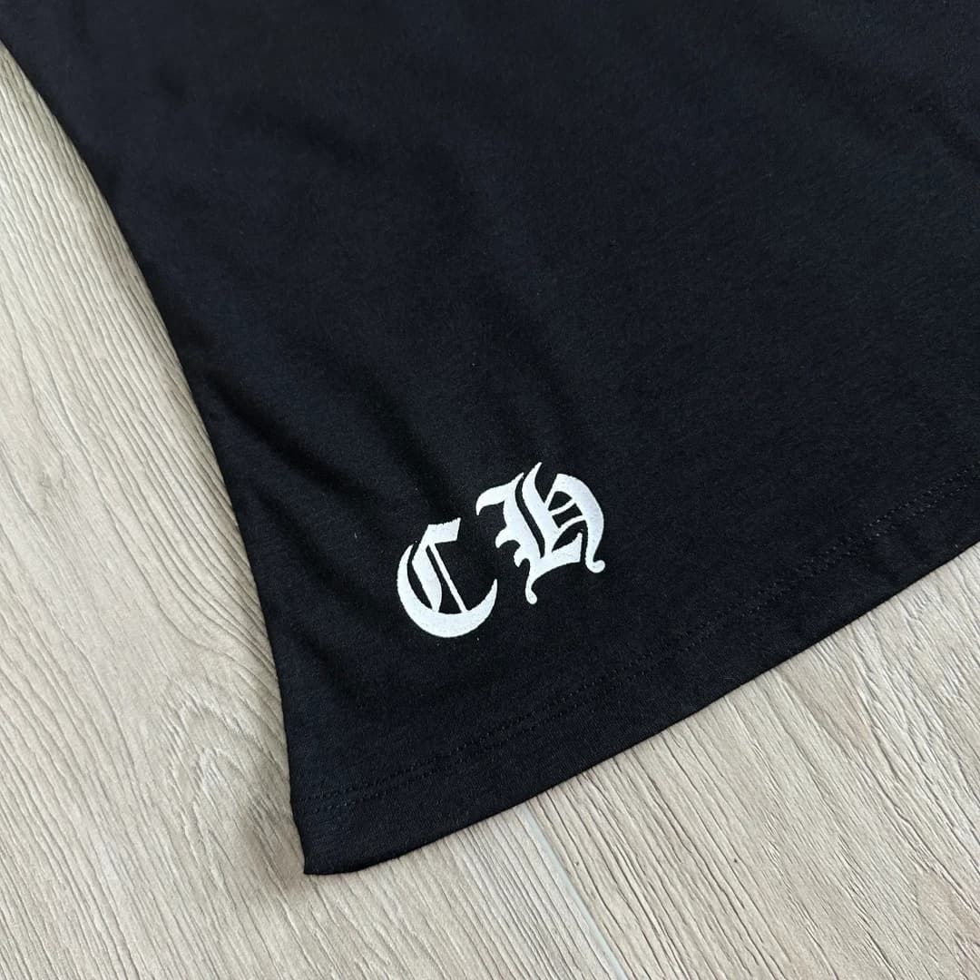Деталь готического логотипа CH на подоле черной футболки Chrome Hearts