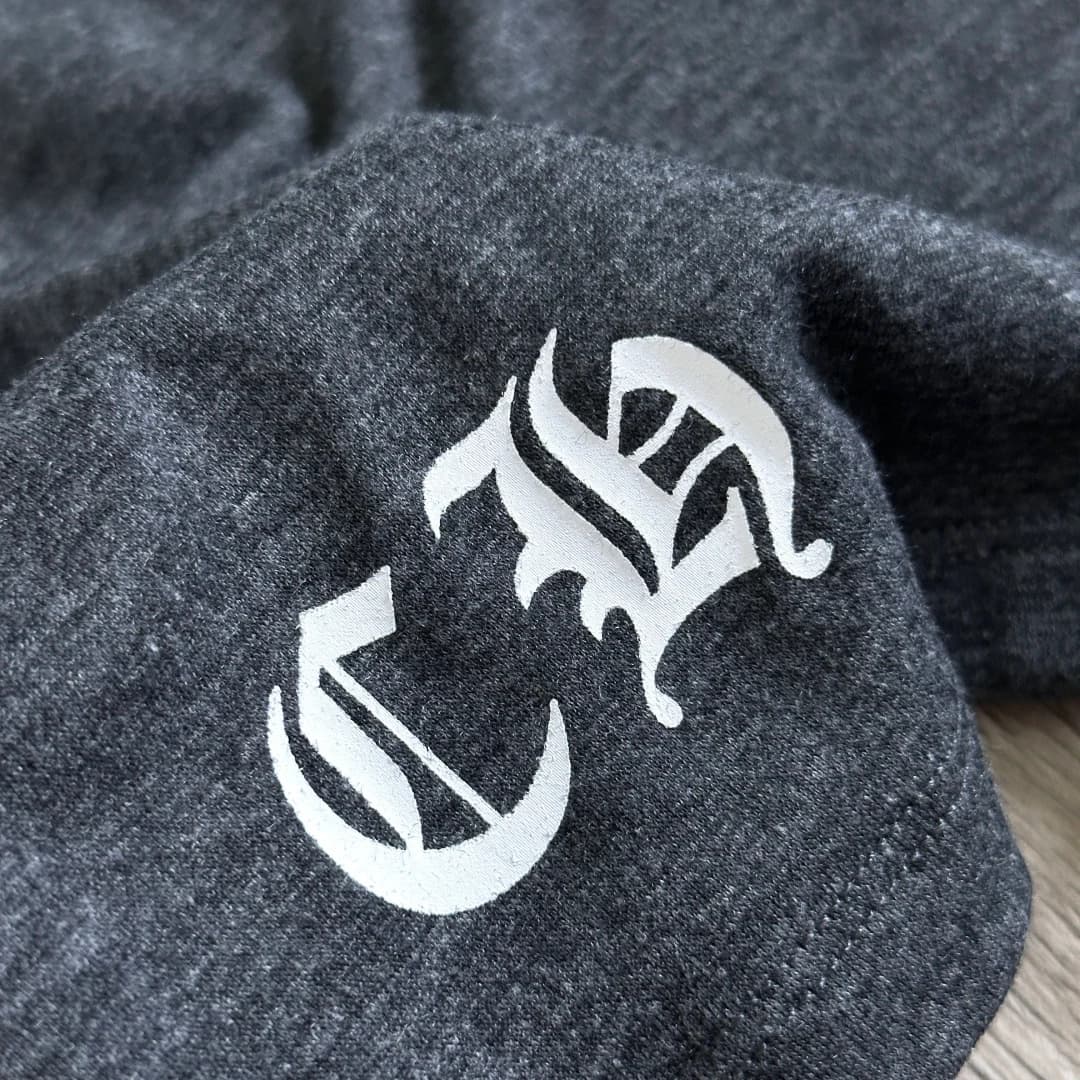 Деталь готического логотипа CH на подоле серой футболки Chrome Hearts