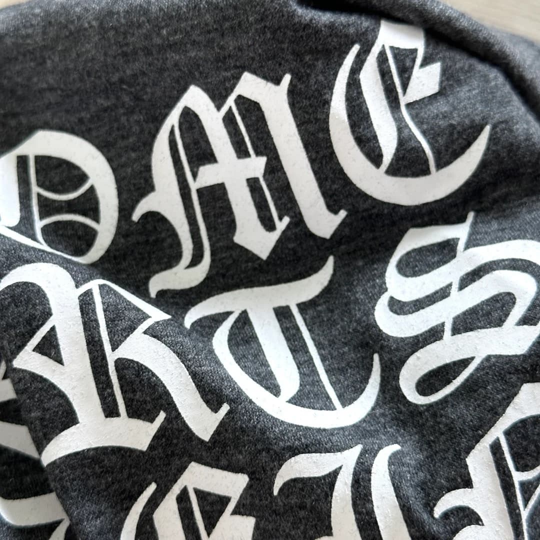 Крупный план готического текстового принта на спине серой футболки Chrome Hearts