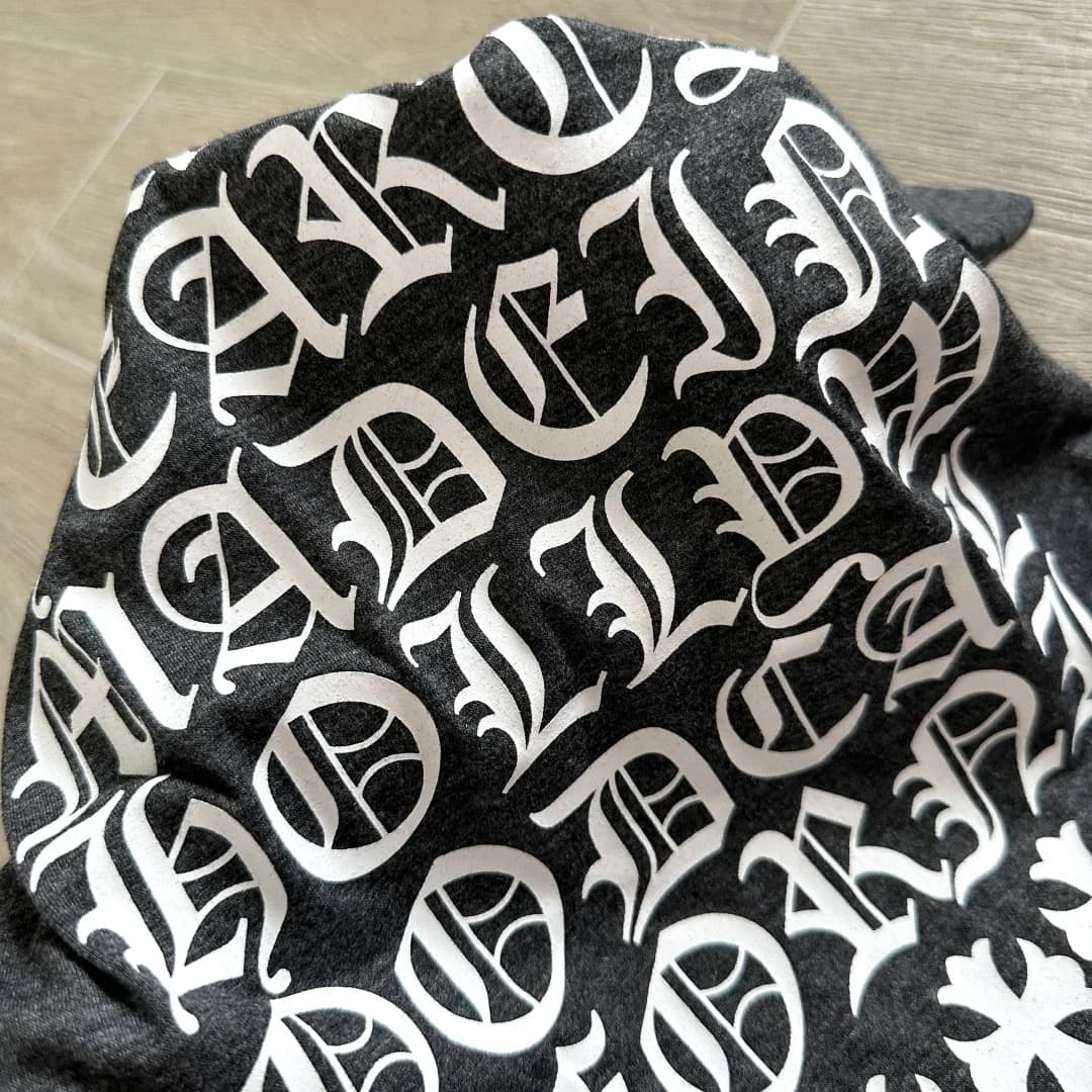 Деталь белого готического принта на серой меланжевой ткани футболки Chrome Hearts