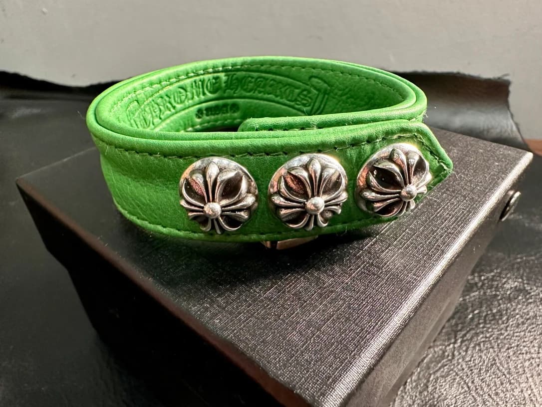 Свернутый зеленый кожаный браслет Chrome Hearts с серебряными заклепками-крестами на коробке