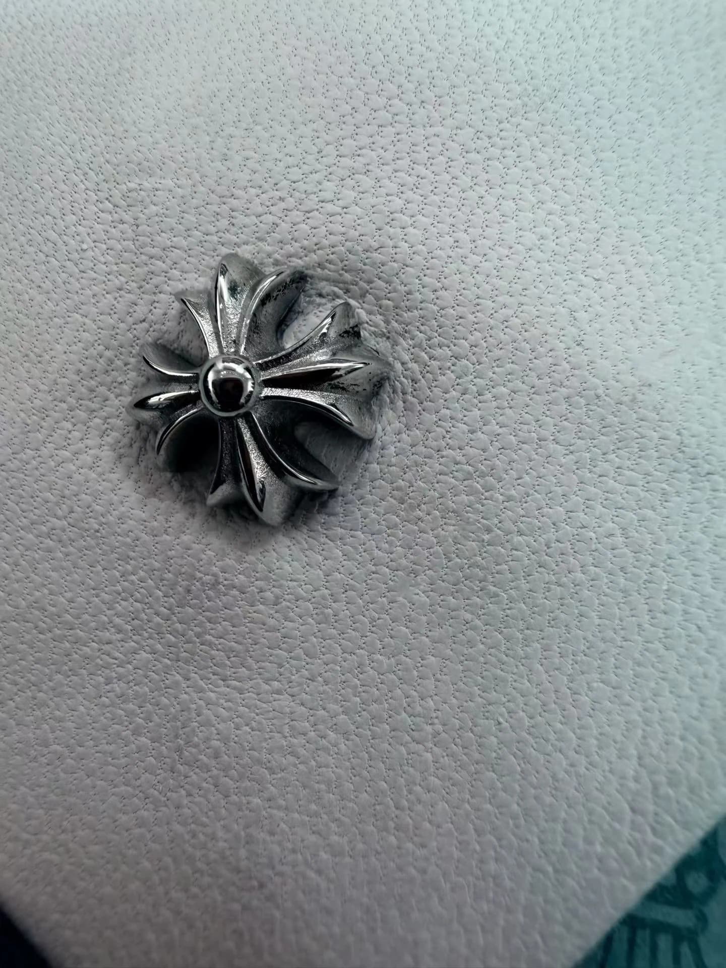 Крупный план серебряной детали в виде креста на белой фактурной коже галстука Chrome Hearts