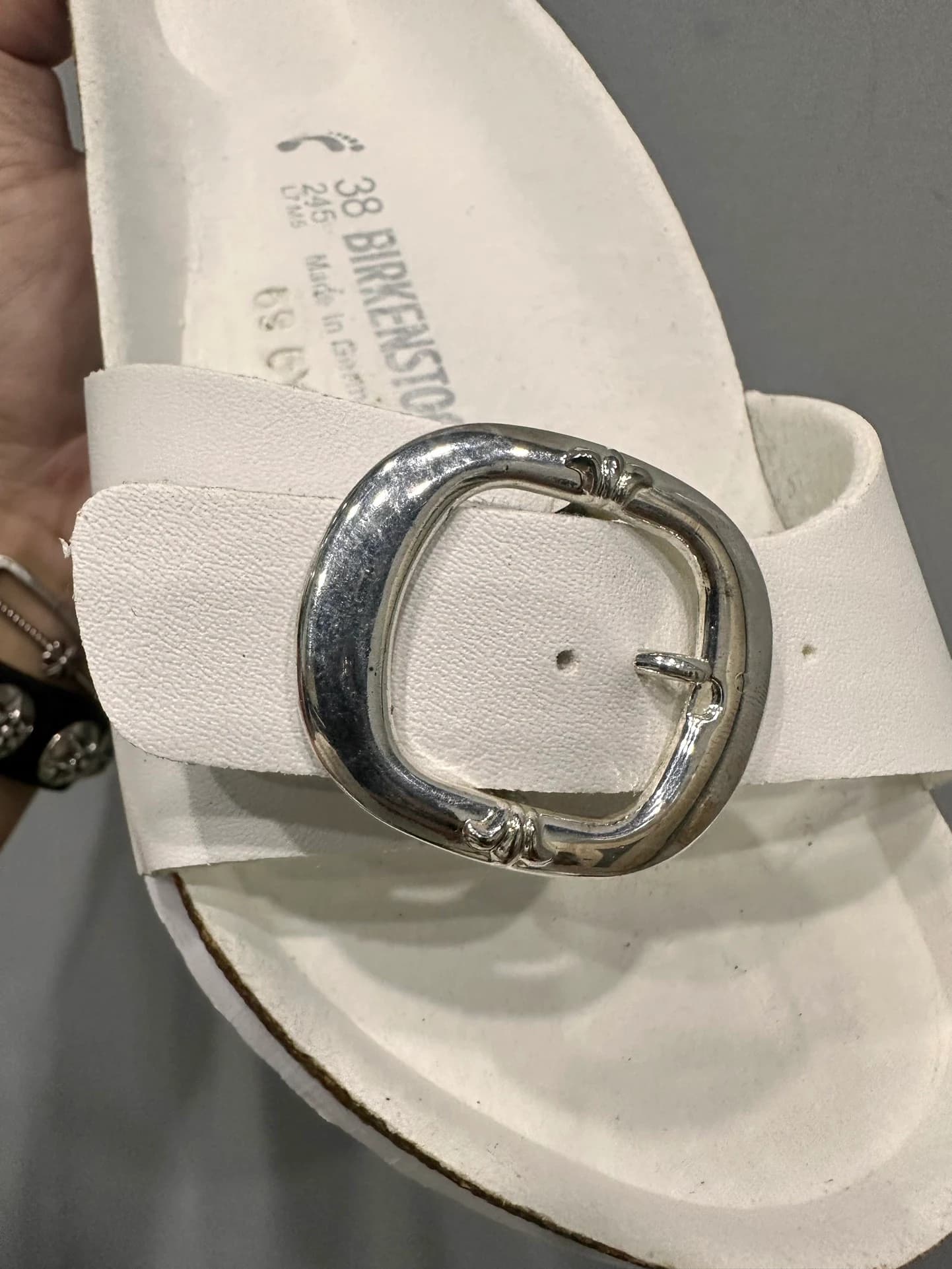 Крупный план серебряной пряжки на белом ремешке шлепанцев Chrome Hearts