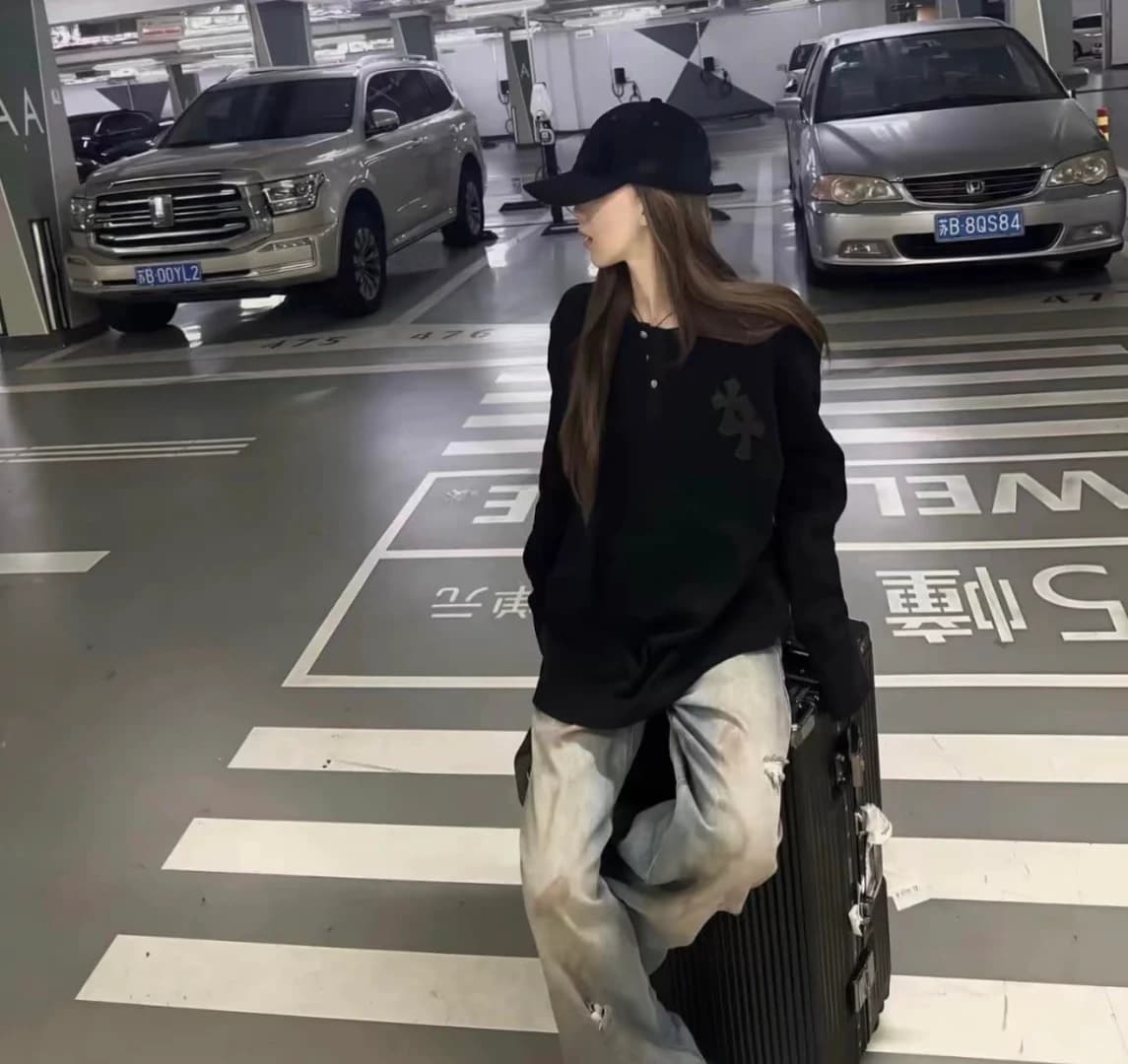 Модель в чёрном лонгсливе и свободных брюках на парковке