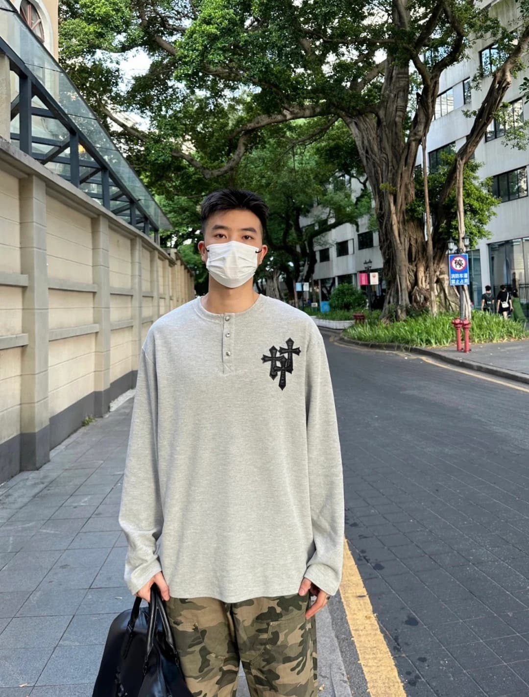 Парень в сером лонгсливе и камуфляжных брюках на улице, вид спереди