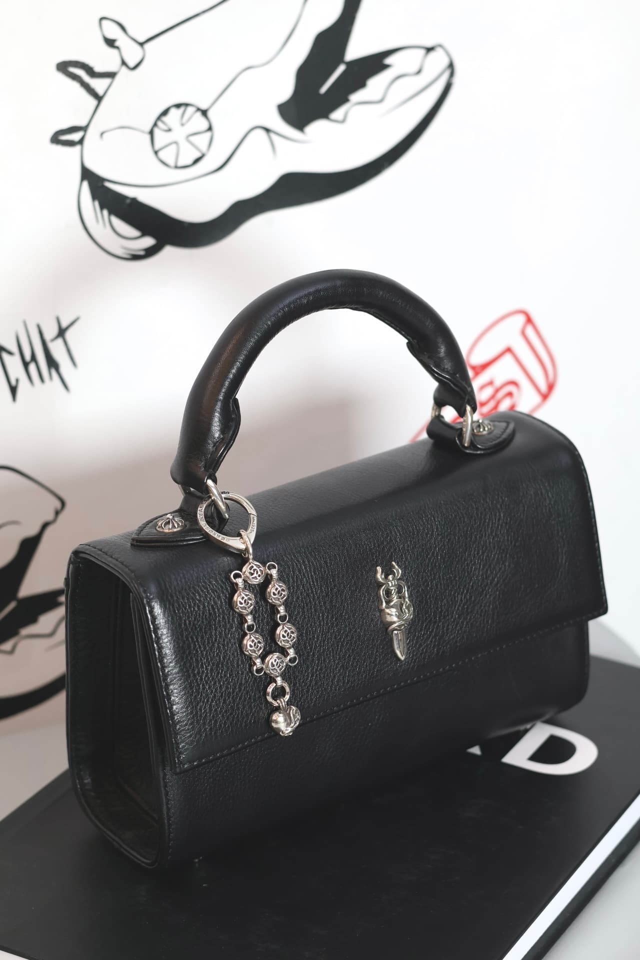 Серебряный кулон Chrome Hearts, закрепленный на ручке черной кожаной сумки