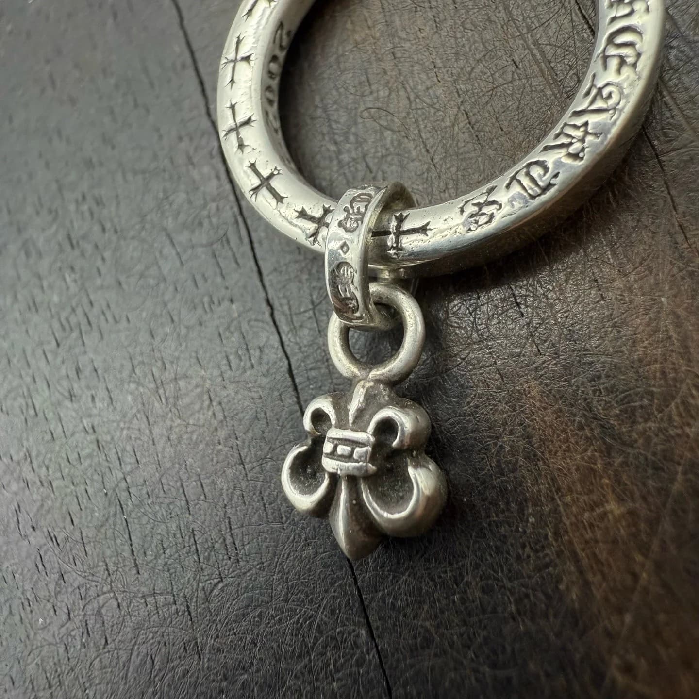 Крупный план серебряной подвески BS Fleur и гравировки на кольце Chrome Hearts
