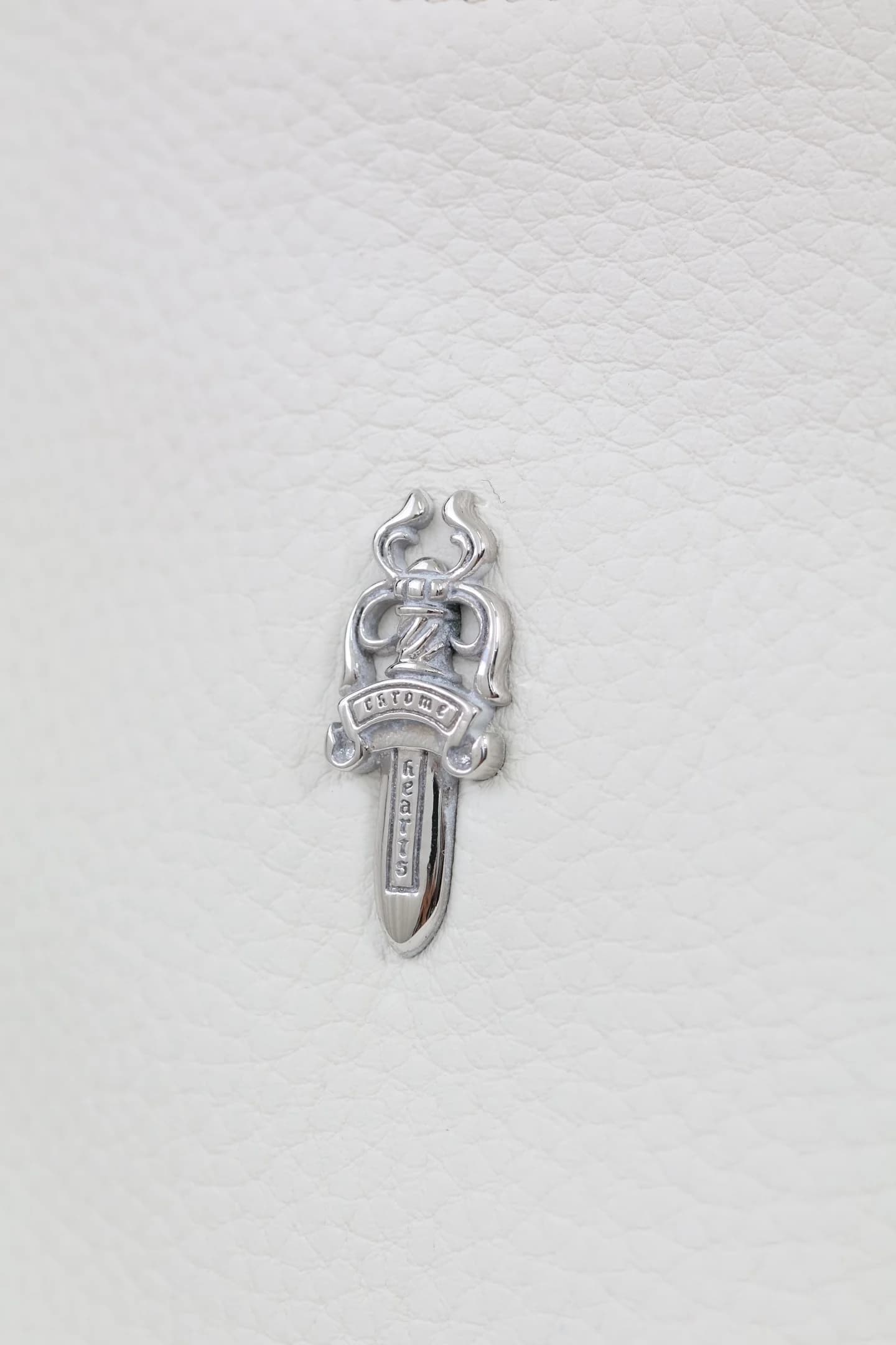 Крупный план серебряной эмблемы в виде кинжала Dagger на зернистой белой коже