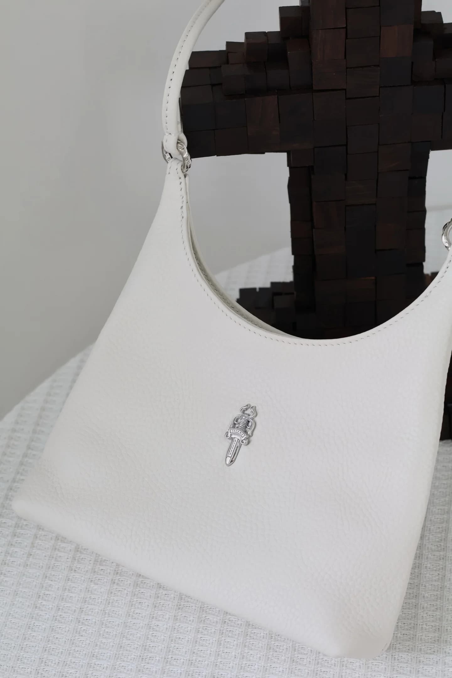 Деталь передней части белой сумки Chrome Hearts с серебряной эмблемой Dagger