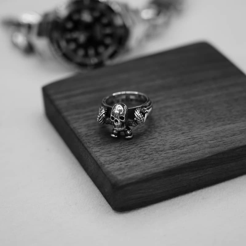 Серебряное кольцо с фигуркой Foti на столе рядом со стеклянным стаканом