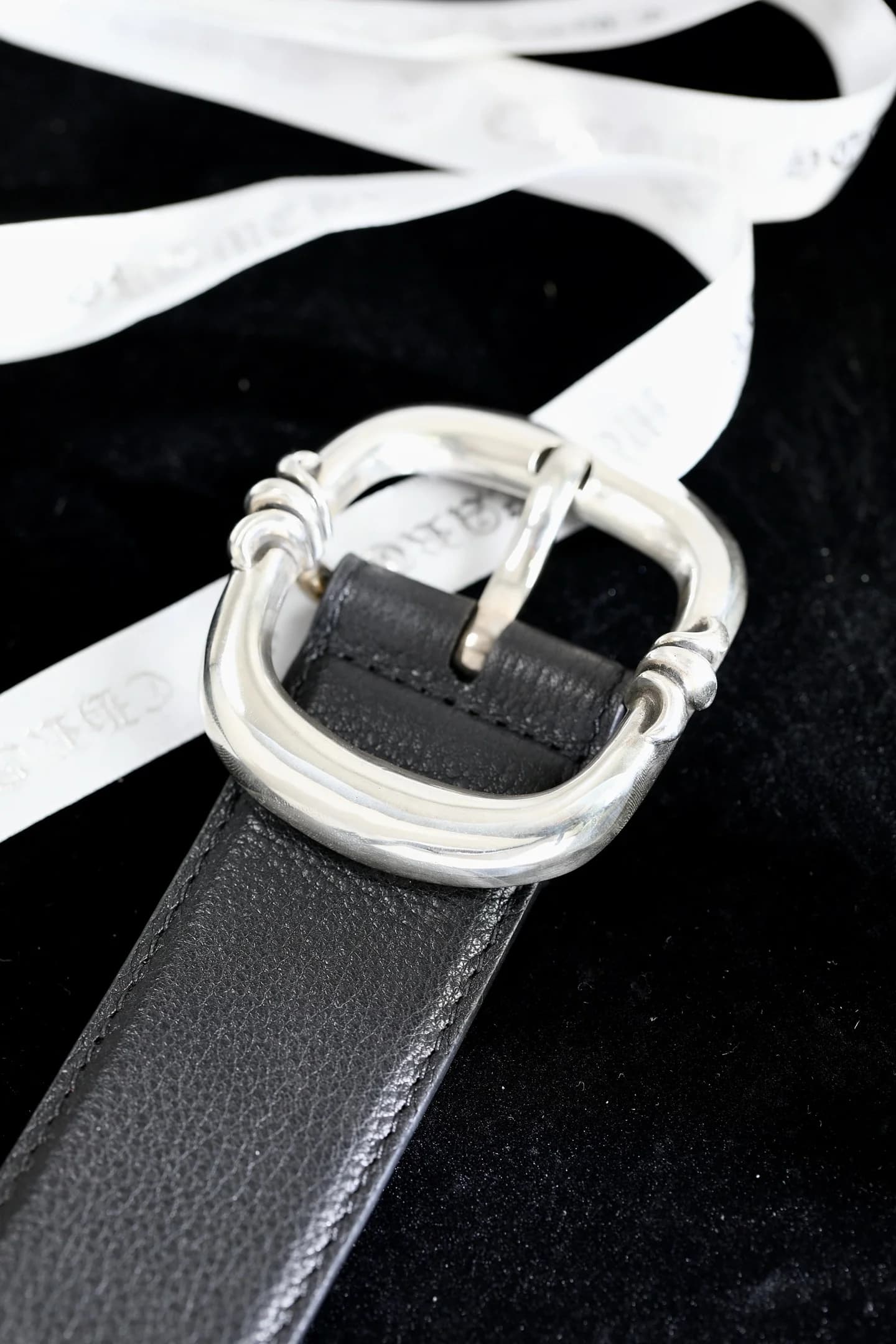 Массивная серебряная пряжка ремня Chrome Hearts на черном фоне с лентой